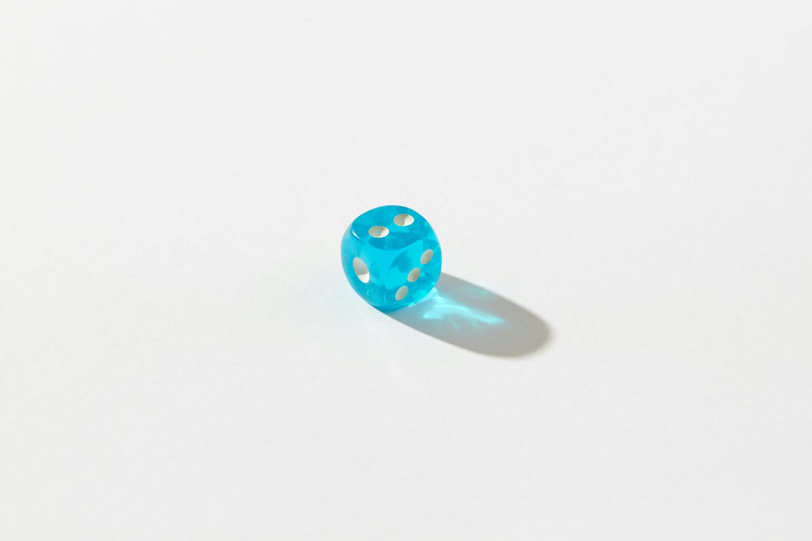 A blue transparent die showing five dots on a white background casting a shadow.